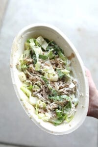 A hand holding a keto chipotle bowl with Carnitas, Romain lettuce, shredded cheese, and sour cream.