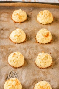 A baking sheet lined with brown parchment paper with two rolls of four coconut macaroons on it.