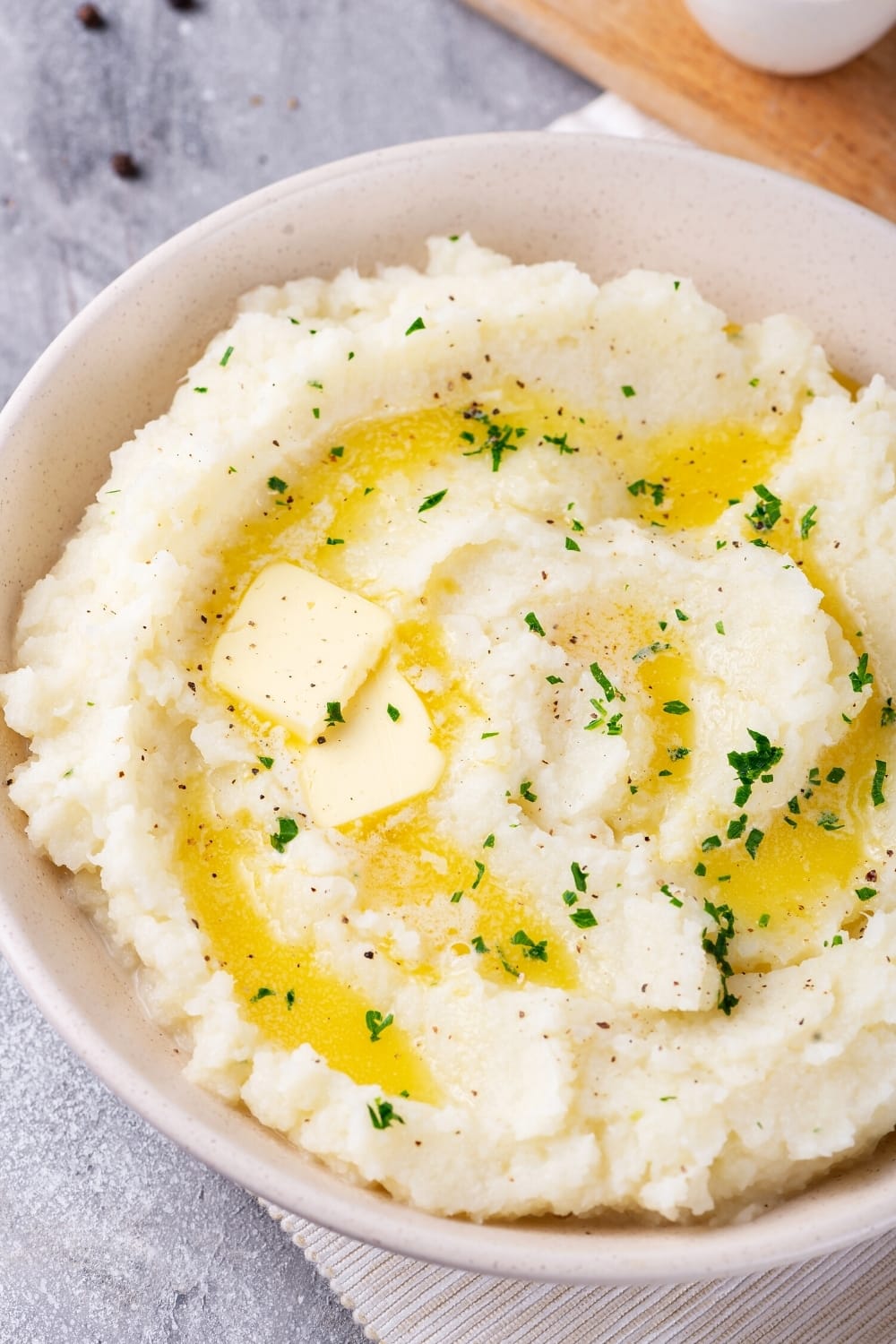A white bowl filled with cauliflower mashed potatoes. The balls on a white tablecloth on a gray counter.