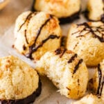 A couple of coconut macaroons on a piece of white parchment paper. One macaroon has a bite out of the front of it showing the inside.