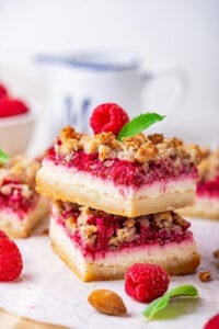 Two raspberry cheesecake bars stacked on top of one another on a piece of white parchment paper.