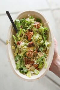 A hand holding a keto chipotle salad bowl with steak, lettuce, and shredded cheese.
