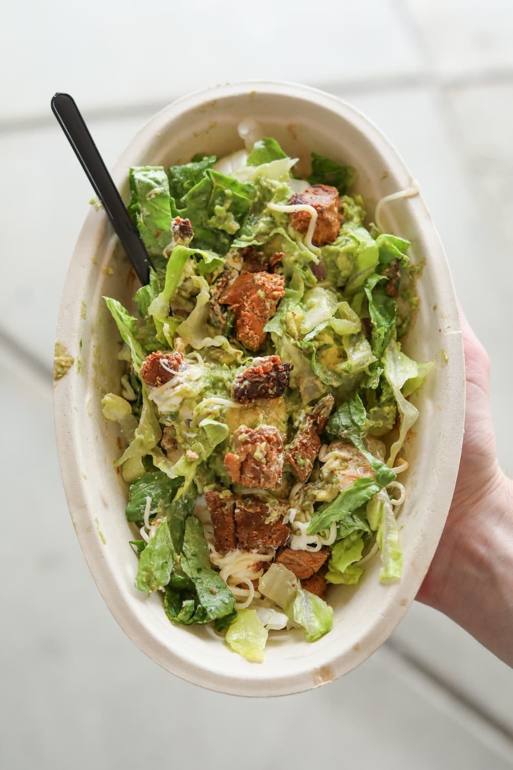 A hand holding a keto chipotle salad bowl with steak, lettuce, and shredded cheese.