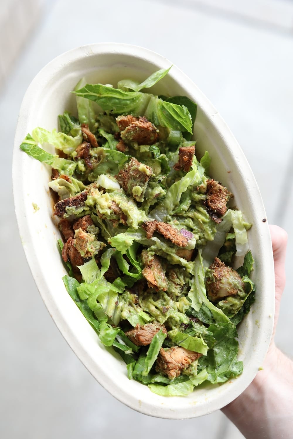 A hand holding a keto chipotle salad bowl with chicken, lettuce, and guacamole.