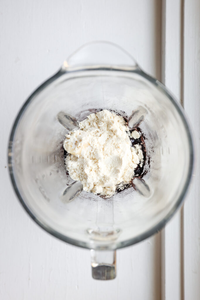 Protein powder, cocoa powder, almond milk, and a banana inside of a blender.