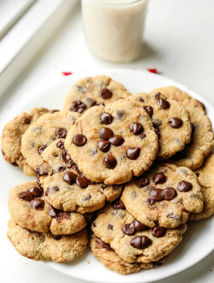 A white plate filled with chocolate chip cookies, and a glass of milk behind it.