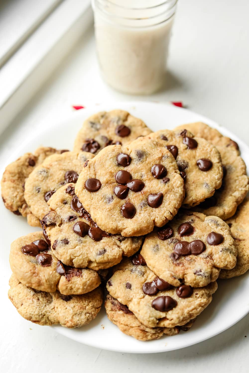 A white plate filled with chocolate chip cookies, and a glass of milk behind it.