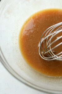A clear bowl filled with a brown butter sauce and a whisk.