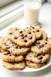 A plate of chocolate chip cookies with a glass of milk set behind the plate.