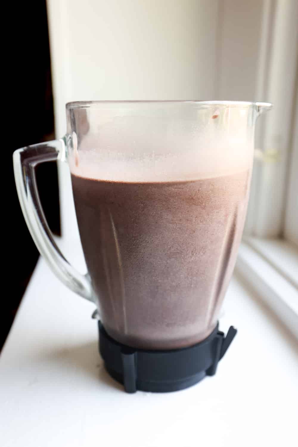 A blender full of a chocolate protein shake on a white counter top.