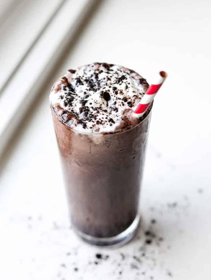 A glass full a chocolate shake. The shake is topped with whipped cream and black cocoa powder.