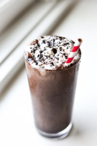 A chocolate shake tops with whipped cream and cocoa powder in a glass.