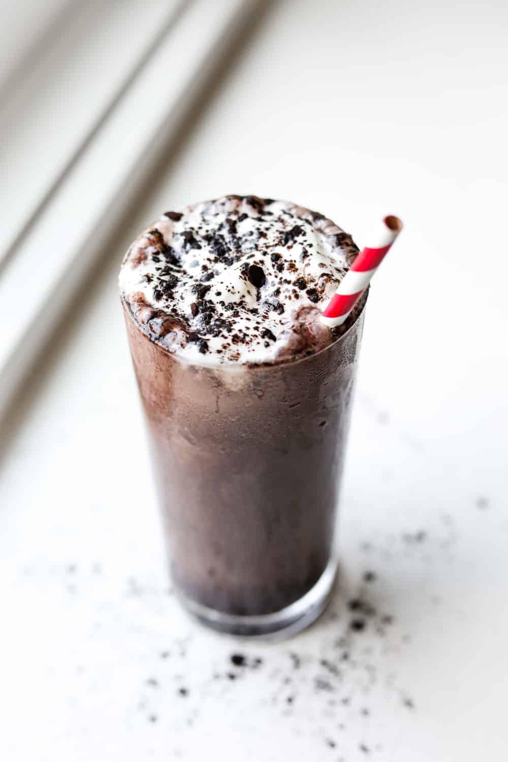 A glass full a chocolate shake. The shake is topped with whipped cream and black cocoa powder.