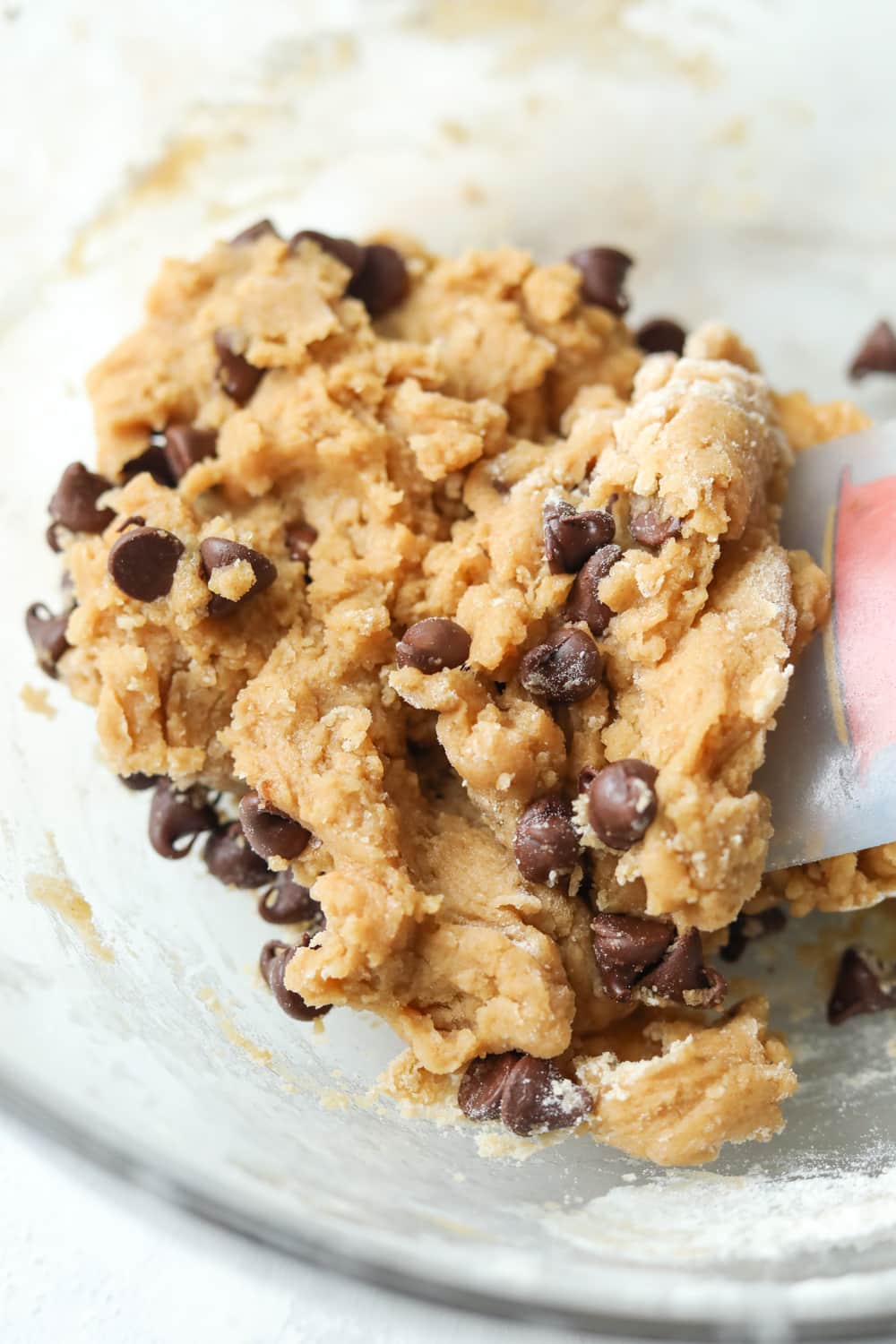 Cookie dough in a clear bowl with a spatula placed inside it.