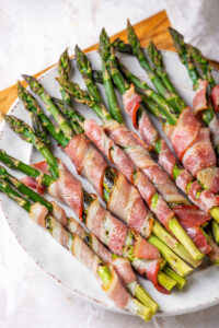 A white plate with bacon wrapped asparagus on it.