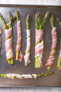 Asparagus wrapped in bacon on a baking sheet.