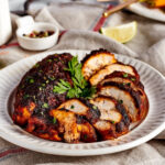 A white plate with a whole piece of blackened chicken breast and a sliced piece of blackened chicken on it.