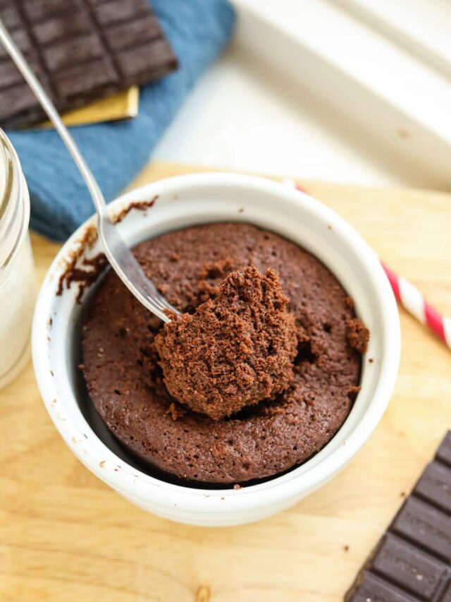 A fork holding a piece of chocolate cake in a white mug.