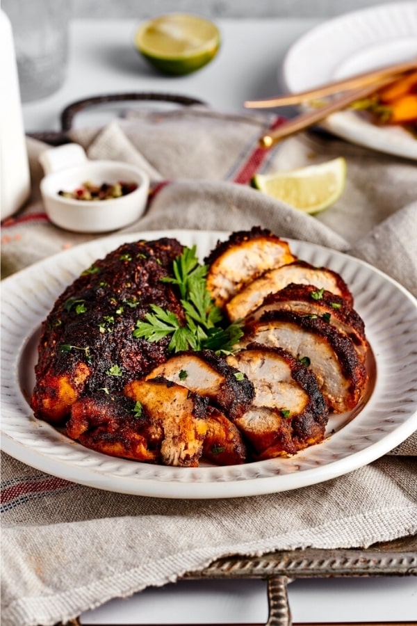 A white plate with a whole blackened chicken breast and a sliced blackened chicken breast next to it.