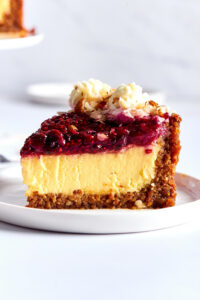 A slice of cheesecake on a white plate on a white counter.