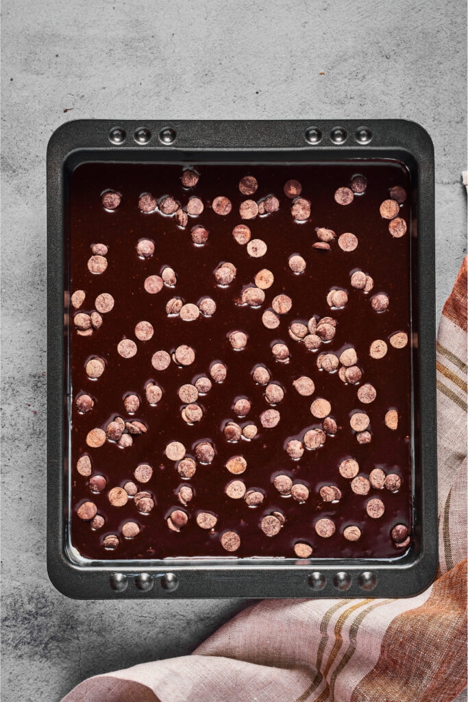 A baking tray filled with brownie batter with chocolate chips on top. The tray is on a gray counter.