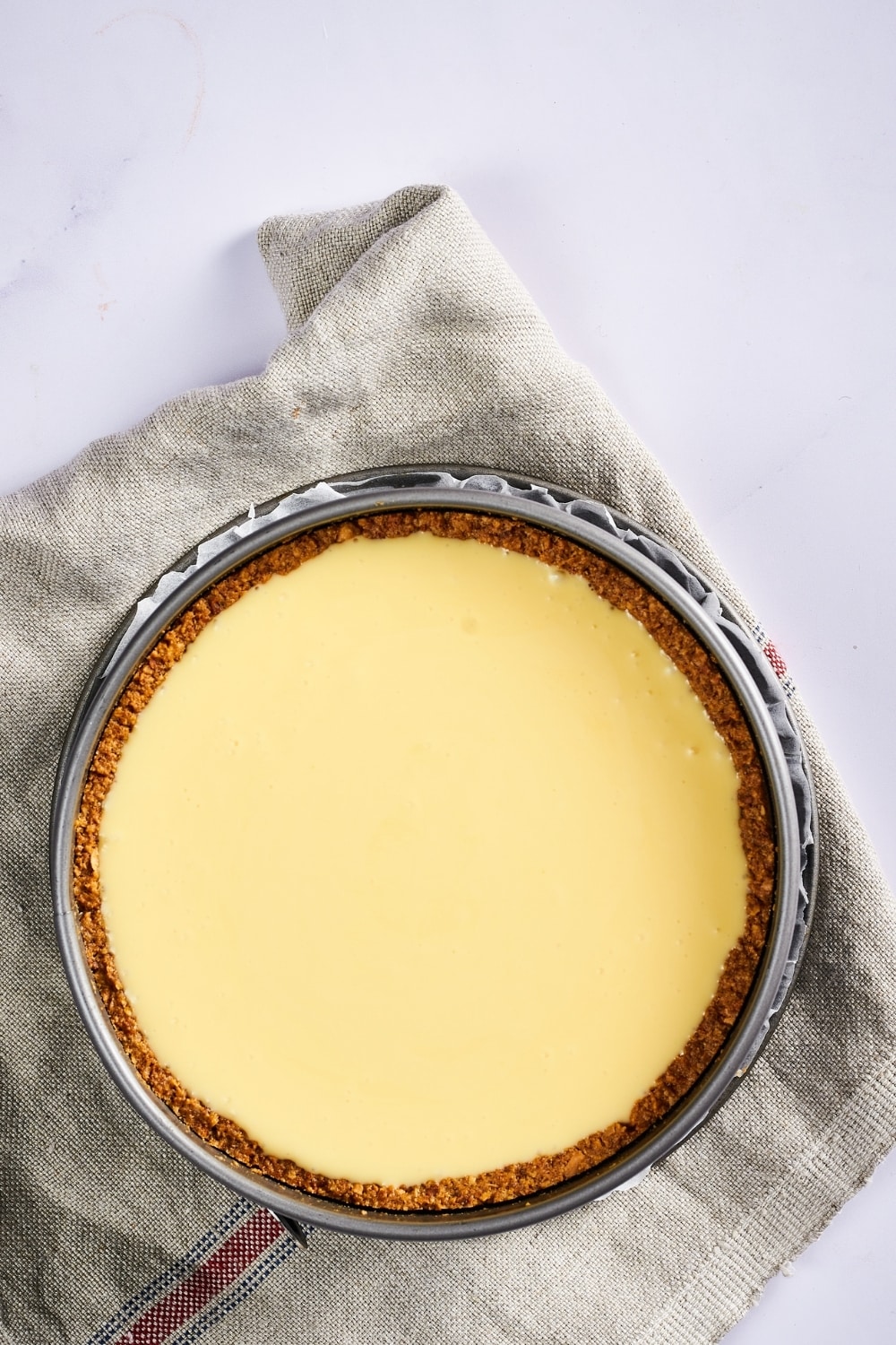 A springform pan filled with an unbaked cheesecake. The pan is on a gray tablecloth on a white counter.