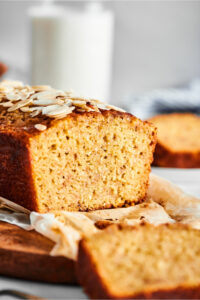 Part of a loaf of banana bread with a slice cut out from the front of it showing the inside of the loaf.