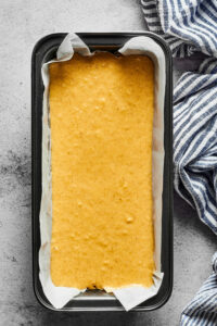 A loaf pan lined with parchment paper with banana bread batter in it. The pan is on a gray counter