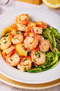 A white bowl with shrimp scampi and noodles in it.