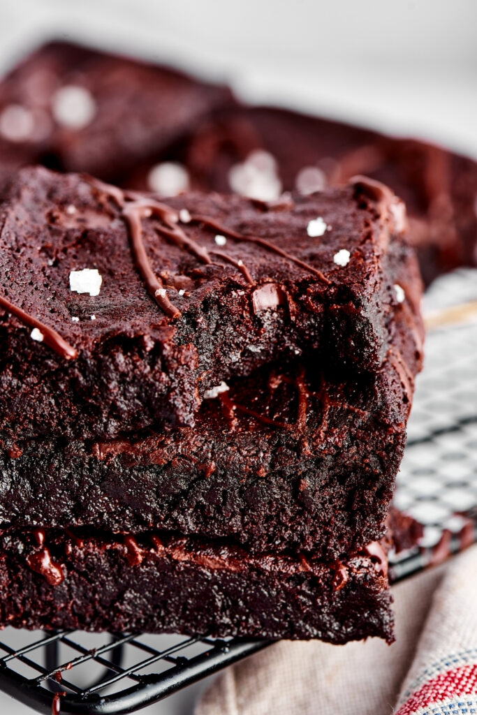 A stack of three brownies on a wire rack. The top Brownie has a bite out of the front right corner of it.