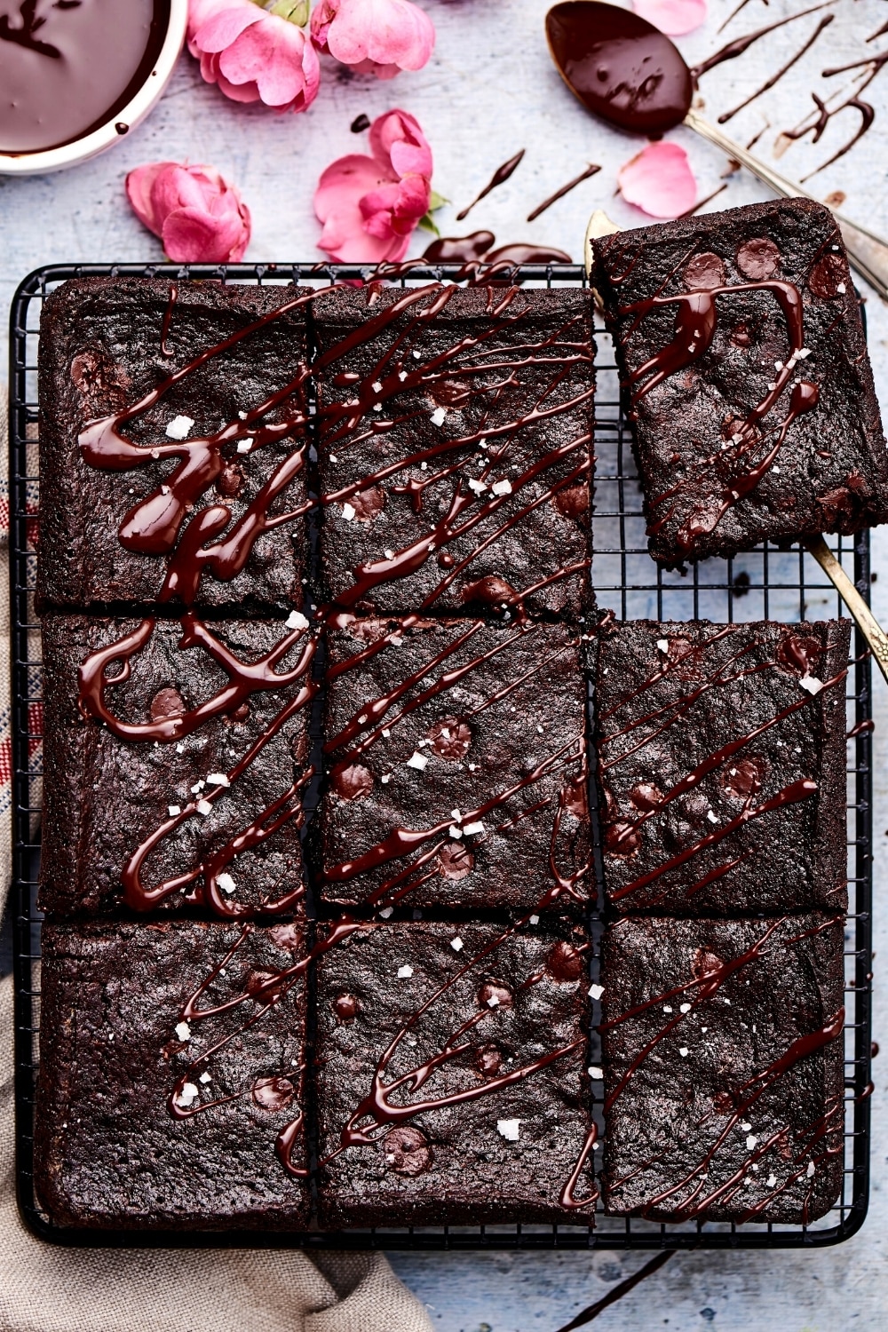 Three rows of three brownies on a wire rack on a gray counter. The top right Brownie is being pulled away from the rest of them with a spatula.