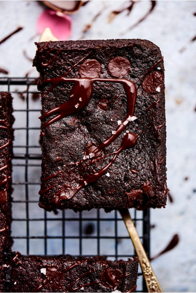 A Brownie is picked up by a serving spatula over a black wire rack.