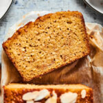 Part of a loaf of banana bread with a slice lying face up in front of it.