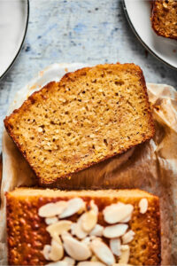 Part of a loaf of banana bread with a slice lying face up in front of it.