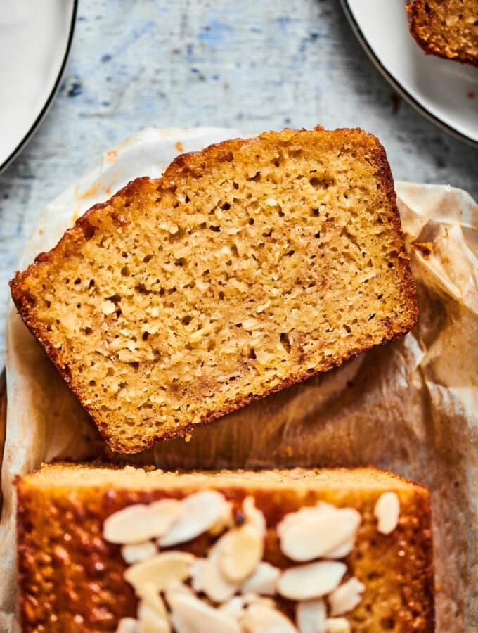 Part of a loaf of banana bread with a slice lying face up in front of it.