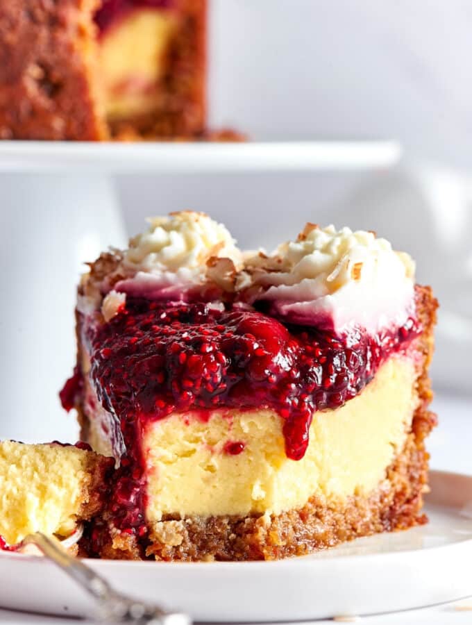 A slice of cheesecake on a white plate that is on my counter. A fork is touching the left the cheesecake and there is a piece from the front of the slice of the cheesecake on the prongs of the fork.