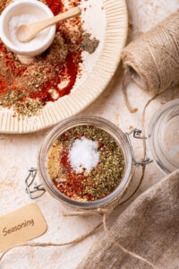 The top of a glass jar with taco seasoning ingredients in it. Behind the jar is part of a white plate with the taco seasoning mixture covering it.