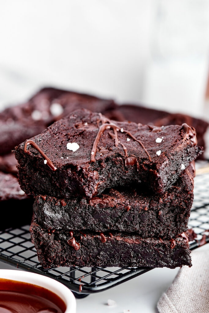 Three brownies stacked on top of one another on a black wire rack. The Brownie on the top has a bite out of the front right of it.