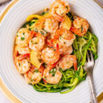 A white bowl filled with zoodles and shrimp scampi. the bowl is on a yellow serving plate on a white counter.