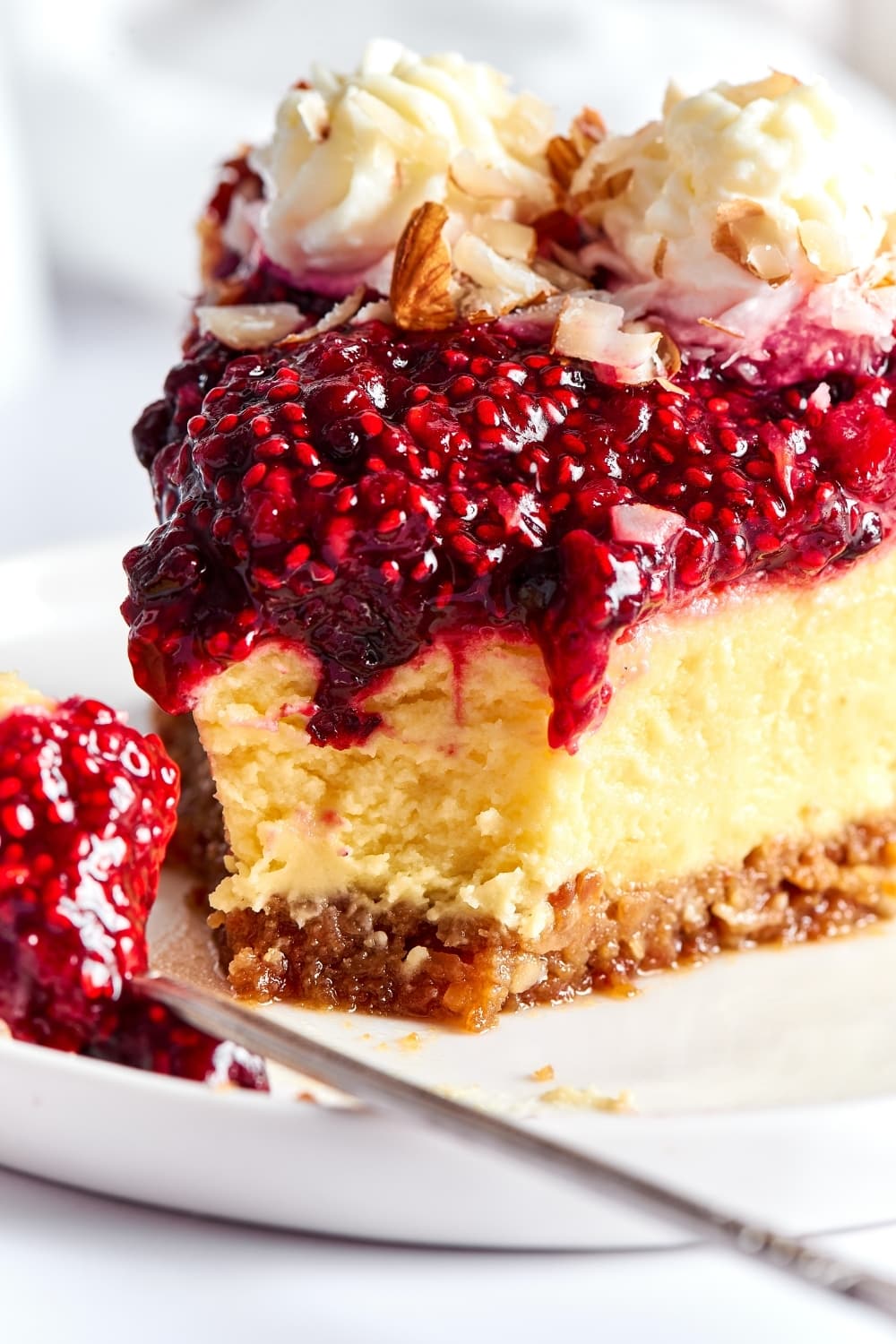 A slice of cheesecake and a white plate. There is a part of cheesecake cut out from the front of it.