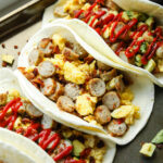 Several breakfast burritos on a gray baking tray.