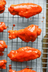 3 Chicken wings covered in hot sauce on a drying rack. One wing is a "drum" and two wings are "flats".