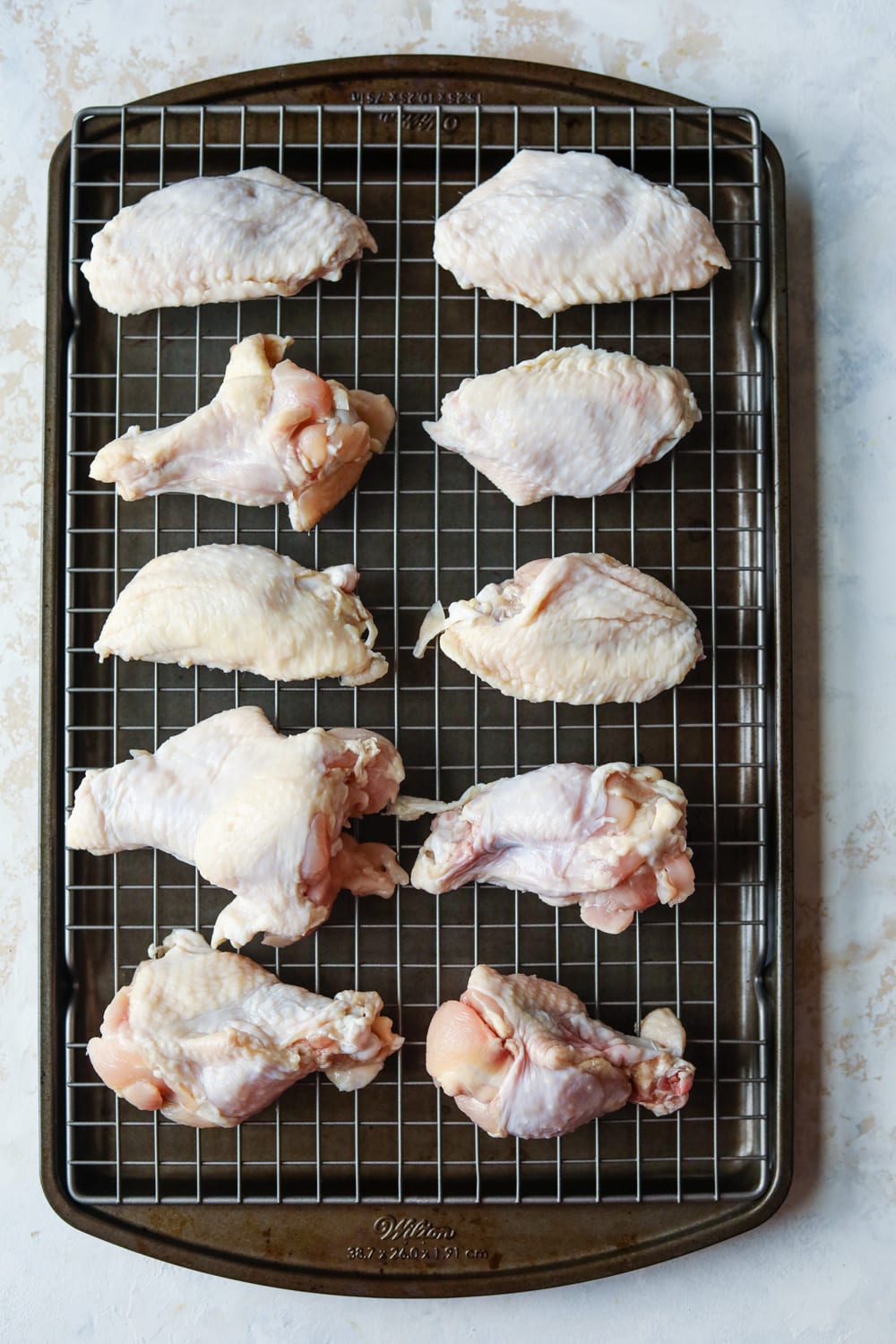 Uncooked chicken wings on a wire rack placed over baking sheet.