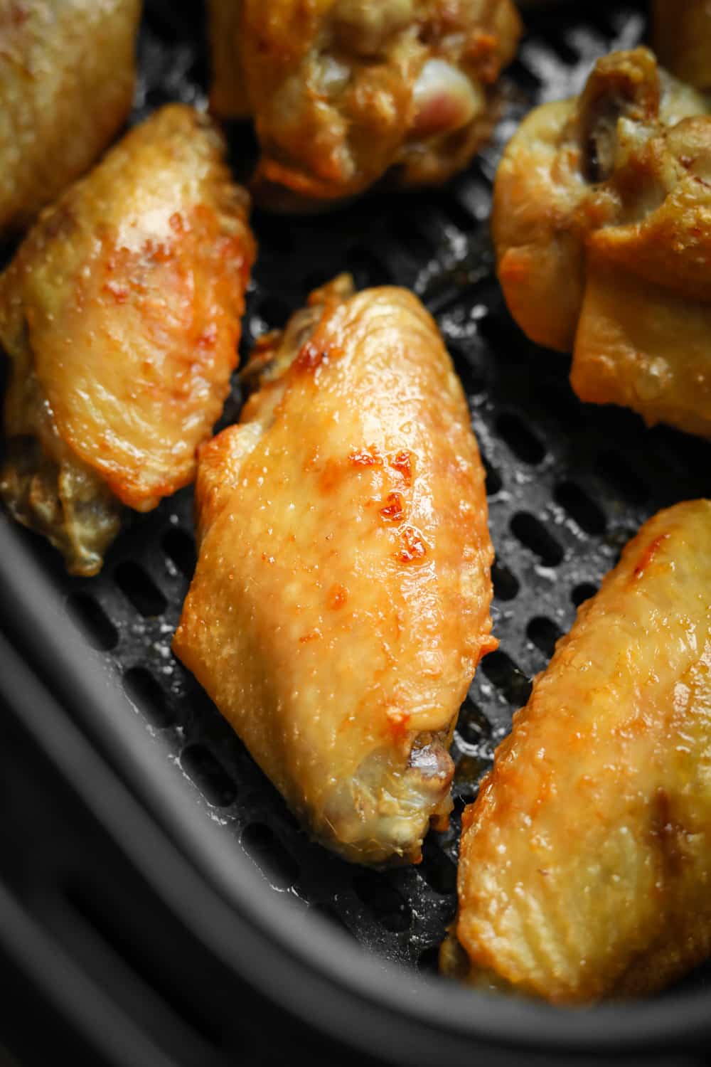 Chicken wings in an air fryer basket that have had multiple intervals of cooking and are ready to be sauced.