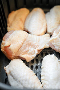 Raw chicken wings in an air fryer basket.