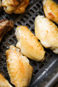 Chicken wings in an air fryer basket that have had 2 intervals of cooking.