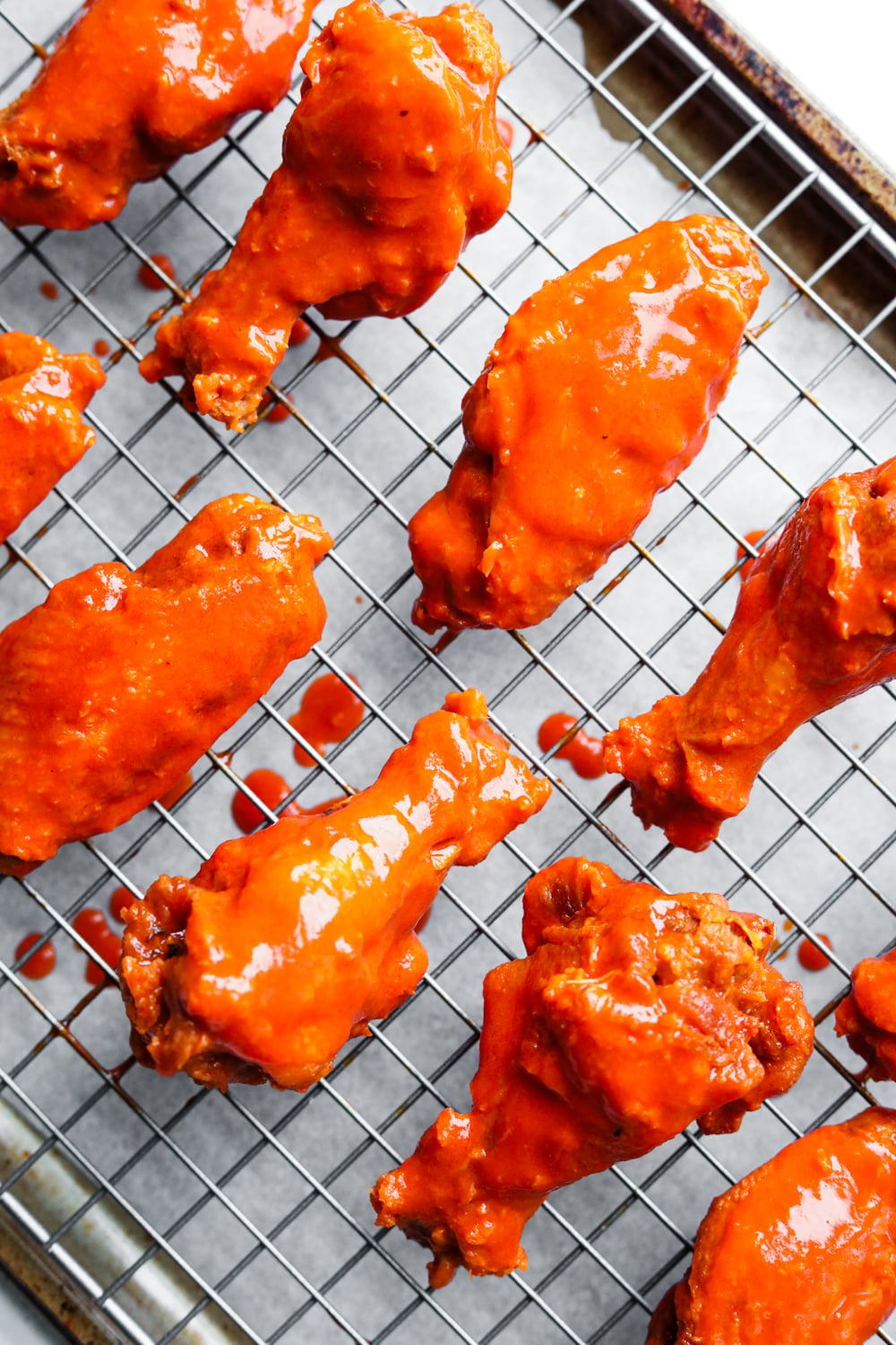 Chicken wings covered in Buffalo sauce on a wire rack.