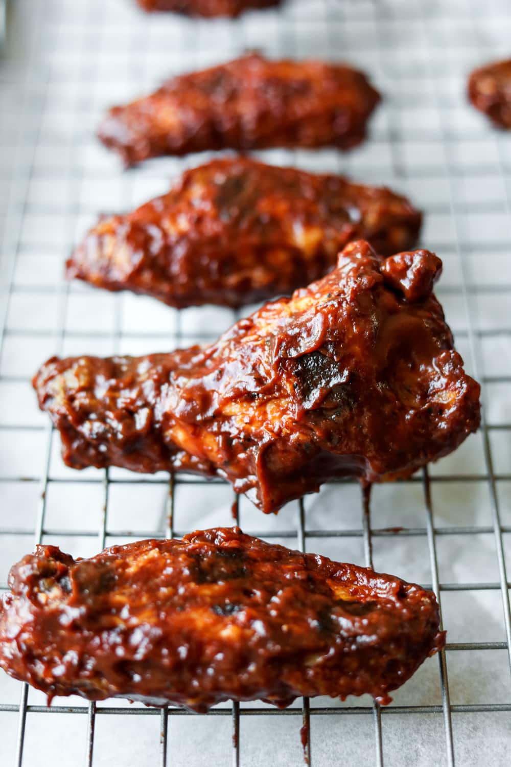 A chicken wing coated in BBQ sauce on a steel drying rack.