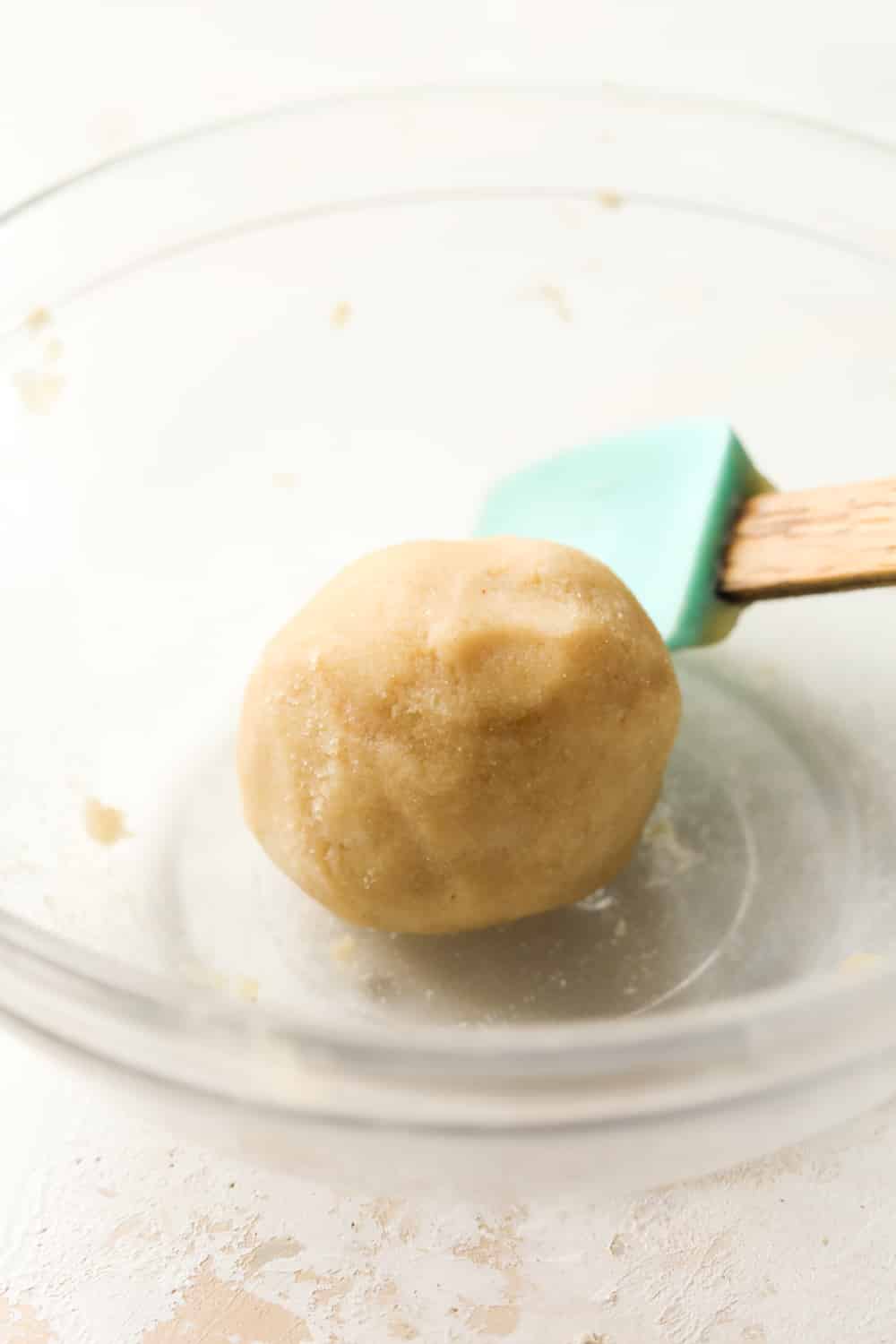 A spatula set next to a ball of dough in a glass bowl.