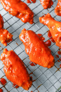 A close up of a "flat" chicken wing on a wire rack. The wing is covered in buffalo sauce.